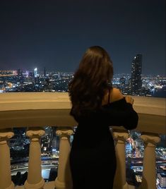 a woman standing on top of a tall building looking at the city lights in the distance