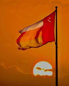 the sun is setting behind a red and yellow flag