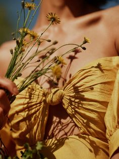 a woman wearing a yellow dress holding flowers in front of her chest and back with one hand