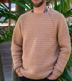 a man standing in front of some palm trees wearing a sweater with holes on it