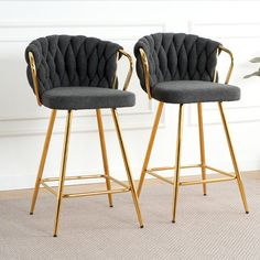 two gray velvet bar stools with gold metal legs and arms in front of a white wall