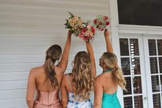 three beautiful women standing next to each other near a white house with flowers in their hands