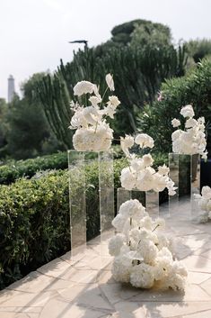 several clear vases filled with white flowers on top of a stone floor next to bushes