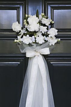 a bouquet of white flowers is tied to a black door with a bow on it