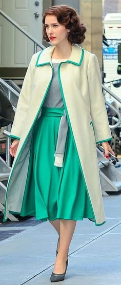 a woman is walking down the street in a green dress and white coat with matching heels