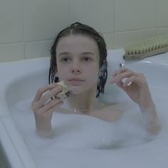 a woman is sitting in the bathtub while brushing her teeth