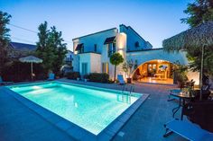 an outdoor swimming pool with lounge chairs and umbrellas next to the house at night