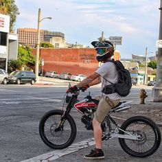 a man with a backpack on his back riding a small bike down the street in front of an intersection