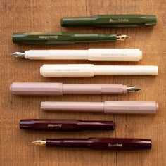 five pens lined up on top of a wooden table