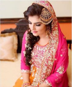 a woman sitting on top of a bed wearing a pink and yellow outfit with gold jewelry