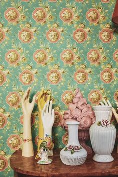 three ceramic vases on a table in front of a wallpapered background with flowers