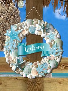 a welcome sign hanging from the side of a wooden fence with shells and starfish on it