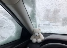 a white teddy bear sitting in the front seat of a car on a snowy day