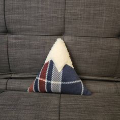 a triangle shaped pillow on the back of a gray couch with a plaid blanket covering it