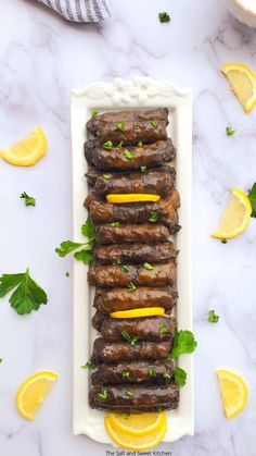 grilled meat with lemons and parsley on a white platter surrounded by sliced lemon wedges