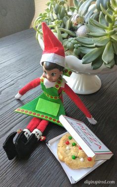 an elf is sitting on the table next to a cookie