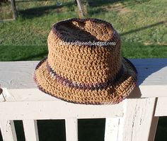 a brown crocheted hat sitting on top of a white fence