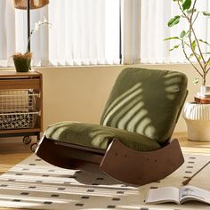 a rocking chair with a book on the floor in front of a window and a plant