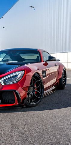 a red and black mercedes sports car parked in front of a white building on a sunny day