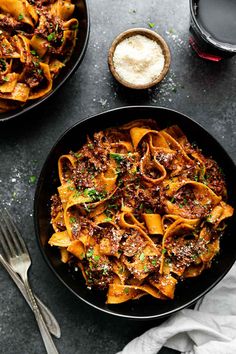 a black bowl filled with pasta and meat on top of a table next to a glass of wine