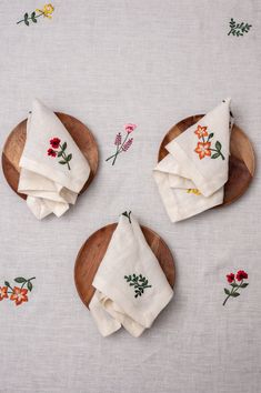 three wooden plates with napkins on them and flowers printed on the table cloth next to each other