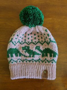 a green and white knitted beanie with an elephant on the front, sitting on top of a wooden table