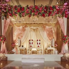 a wedding stage decorated with pink flowers and white linens, gold chairs and chandeliers