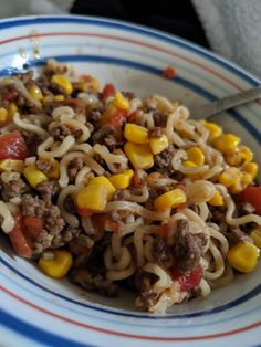 a bowl filled with noodles, meat and corn on top of a blue and white striped plate