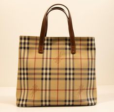 A Burberry handbag/shopper made of vinyl coated canvas with the Burberry classic check and brown leather finish. The interior is lined with black fabric, and next to the major compartment it features one side pocket with a zipper. The bag will be delivered with its Burberry dust bag. The condition is very good with hardly any signs of use.  Dimensions:  Width:29 cm Height:26.5 cm Depth:10.5 cm We ship within 1-3 working days. The items are packed very well to prevent any damage during the transp Burberry Handbag, Burberry Classic, Leather Finish, Top Handle Bags, Burberry Handbags, Side Pocket, Black Fabric, Leather Trims, Purses And Handbags