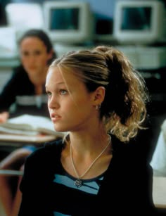 a woman sitting at a desk in front of a computer monitor with another person behind her