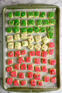 a baking sheet filled with green and red sugar cubes on top of a marble counter