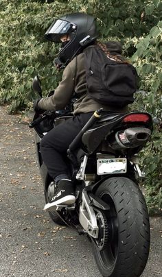 a man riding on the back of a motorcycle down a road next to bushes and trees