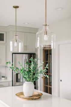 a white kitchen with an island and glass pendant lights hanging from the ceiling over it