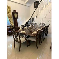 a dining room table set with place settings in front of the staircase and clock on the wall