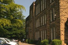 several cars parked in front of an old brick building on a street with tall trees