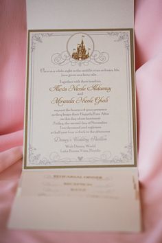 a wedding card with a castle in the middle on pink satin material and gold trim