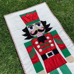 a green and red quilt with a nutcracker on it sitting in the grass