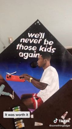 a man sitting on top of a bed next to a giant kite that reads well never be those kids again