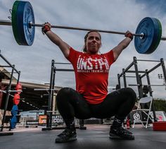 a woman squats on the ground while holding two barbells above her head