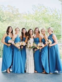 a group of women standing next to each other wearing blue dresses and holding bouquets