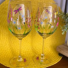 two hand painted wine glasses sitting on top of a yellow place mat next to a potted plant