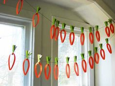 some paper carrots are hanging from a string in front of a window with two windows