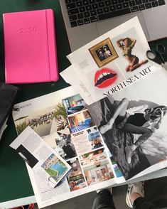 an open magazine sitting on top of a desk next to a laptop and a pink notebook