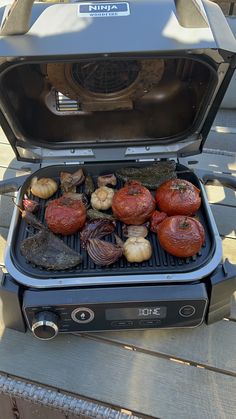 an outdoor grill with various foods cooking on it's side and the lid open