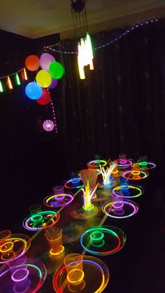 a table topped with lots of neon colored plates and cups filled with liquid on top of it