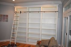 a living room filled with lots of white bookshelves next to a ladder in front of a window