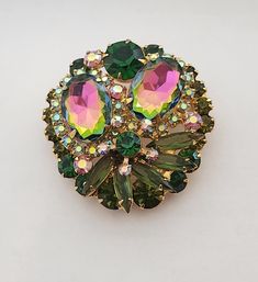 Stunning Juliana also known by name DeLizza & Elster Brooch in very good pre-loved condition.  Measures 1 3/4" in diameter. Brooch is featuring  two larger watermelon rhinestones (they mix of green and pink colors)  dark green,  olivine, pink  and Aurora Bareilles rhinestones. Brooch is identified for being Juliana by construction and setting of the stones. The original was sold with paper hang tag was used on jewelry and most likely was discarded by original owner.  Juliana jewelry was named after Frank DeLizza mother.  This style was always carried by DeLizza & Elster. Highly collectable.  Perfect for any occasion. Juliana Jewelry, Green And Pink, Rhinestone Brooches, Hang Tags, Antique Jewelry, Halloween Shopping, Bead Work, Pink Color, Vintage Antiques