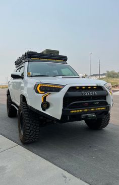 the front end of a white toyota truck with its lights on, parked in a parking lot