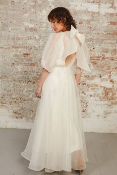 a woman in a white dress standing against a brick wall with her back to the camera