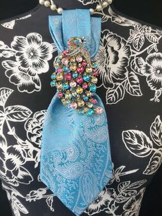 This Blue Paisley Necktie Necklace is made with a  woven silk tie, and features a Multi Color Rhinestone Peacock Brooch strung on your choice of an adjustable Rosary Chain Ribbon Tie Pearl Necklace or an adjustable Elastic Band. The soft, comfortable fabric sits perfectly on any size chest, while the adjustable necklace feature allows you to customize the fit to your liking. Measuring at a versatile length, this necktie necklace is designed to be a one-size-fits-all. View all Women Tie's: https://www.etsy.com/shop/FearlessAccessorizer?ref=seller-platform-mcnav§ion_id=49097355 The single strand of pearls is an easy and fashionable way to wear this tie necklace. Looks really cute on a t-shirt or a blouse. All jewelry is individually handmade solely by me the designer and owner of Fearless & Women's Neck Ties, Outfit Feminine, Peacock Brooch, Tie Ideas, Women Necktie, Diy Tie, Tie For Women, Tie Necklace, Women Ties